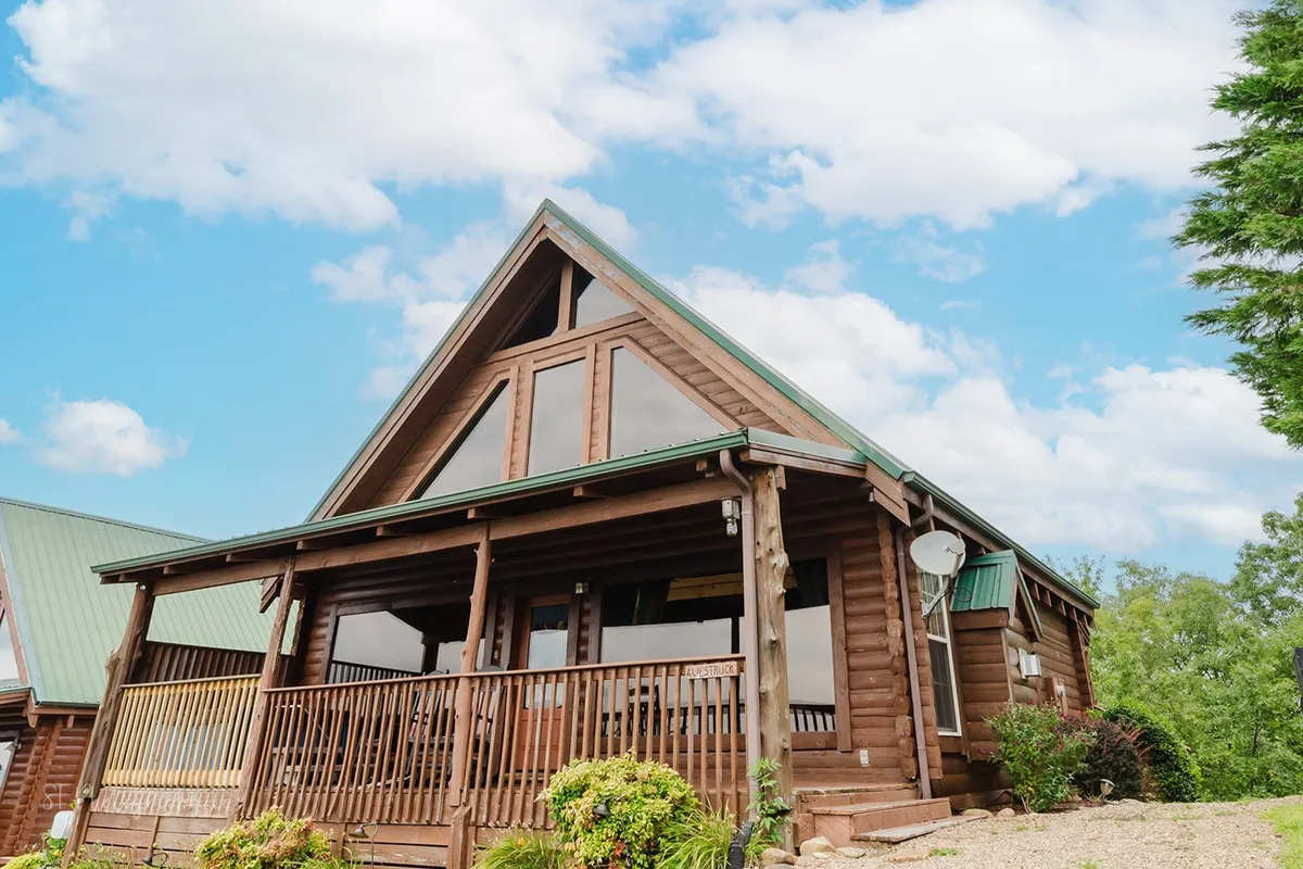This image shows the log cabin exterior with large windows and a green roof, surrounded by natural landscaping. The inviting porch suggests a place to gather before or after venturing out to nearby attractions, embodying the spirit of a mountain retreat.