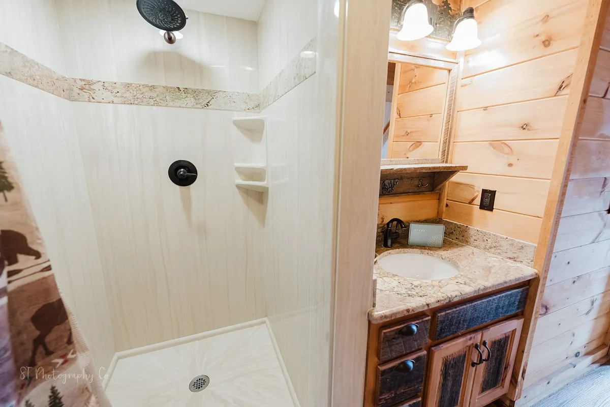 This inviting bathroom features a modern walk-in shower, vanity with sink, wooden wall panels, and soft lighting. The space exudes a feeling of relaxation and rejuvenation, ideal for self-care after a long day of adventure.