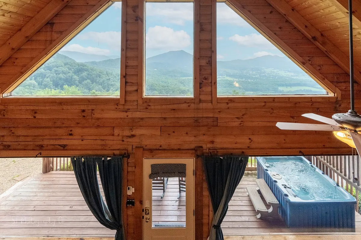 A cozy dining area with large windows offering stunning mountain views, a hot tub, and rustic wooden beams. The setting combines opportunities for relaxation and socializing, with the bonus of enjoying the scenery from indoors or the hot tub, perfectly embodying a value-packed getaway.