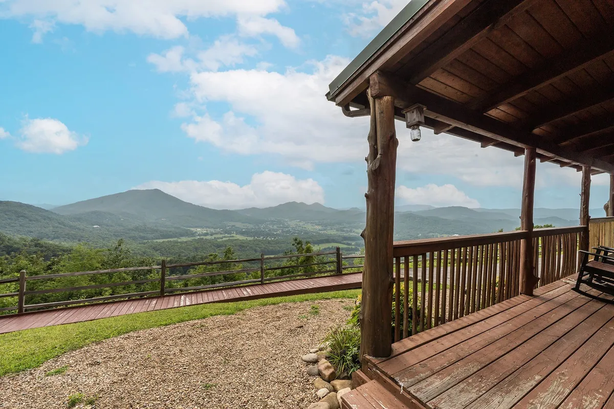 A wide wooden deck with comfortable seating overlooks expansive mountain views, surrounded by natural landscaping. The tranquil scene is set during sunrise or sunset, with mist gently rolling over the peaks. The deck invites relaxation, stargazing, and outdoor gatherings while immersing you in the beauty of the Smokies.